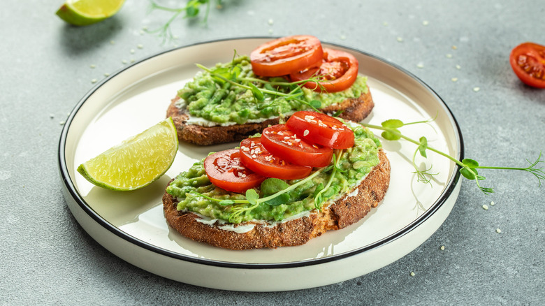 Two avocado toasts topped with sliced tomatoes