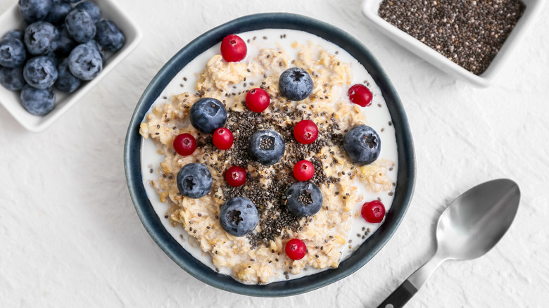 Top view of bowl with oatmeal, chia seeds, and berries on white background