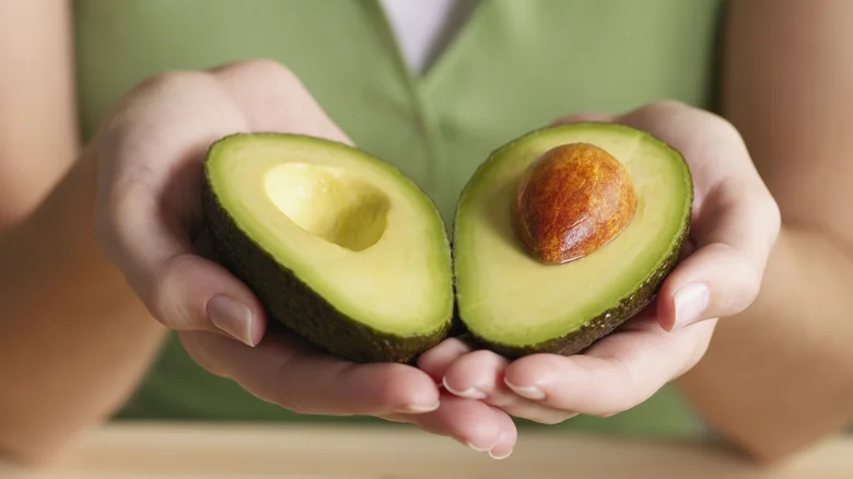 Woman holding two ripe avocado halves