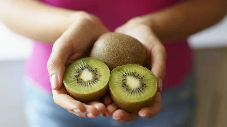 Woman holding one whole kiwi and two kiwi halves