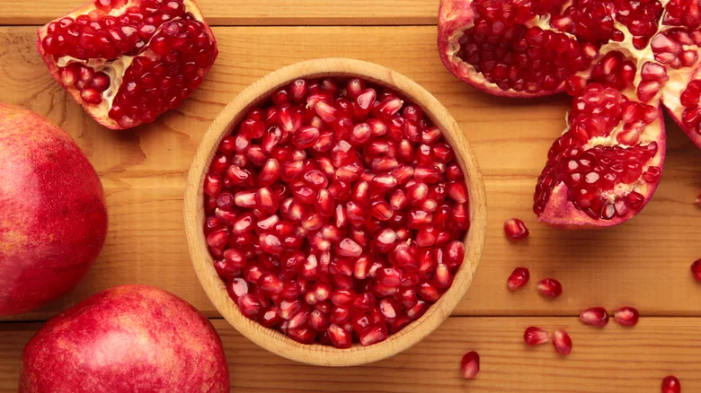 Top view of open pomegranates, and pomegranate seeds on wooden background