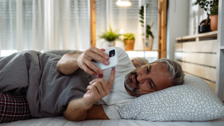 Middle-aged man lying in bed and using a smart phone
