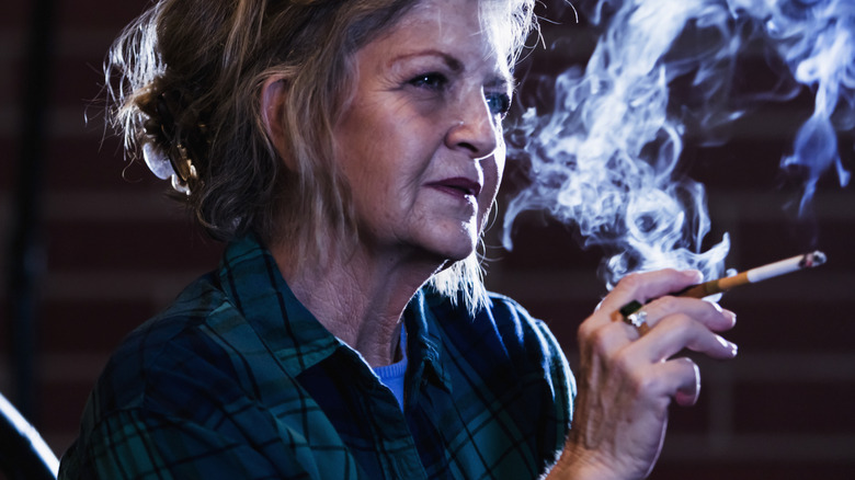 Senior woman smoking cigarette in a dark room