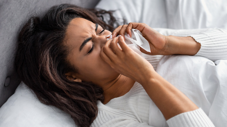 woman blowing nose in bed
