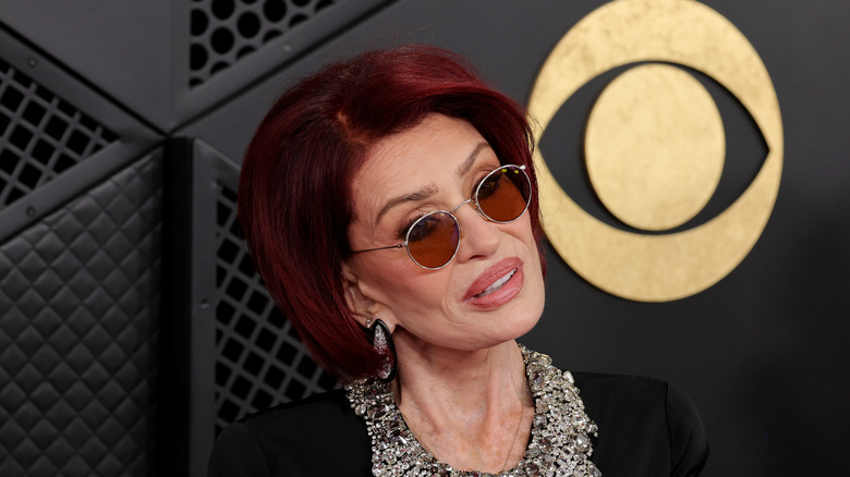 Sharon Osbourne wearing round sunglasses and black dress with jeweled neckline