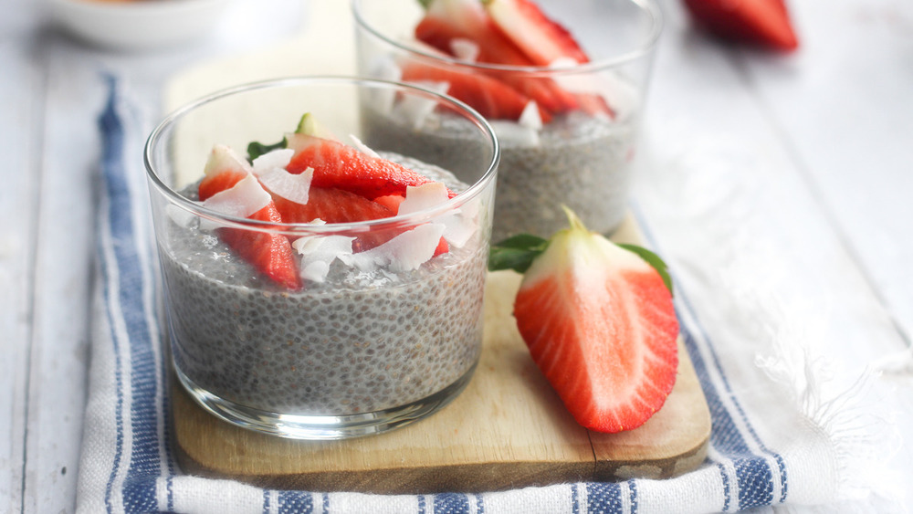 Glass cup of chia seed pudding with sliced strawberries and coconut flakes