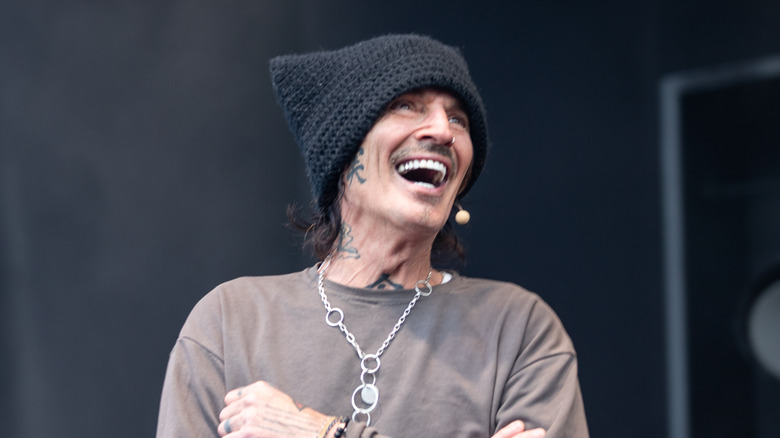 Tommy Lee laughing on stage wearing a knitted hat and long-sleeved t-shirt