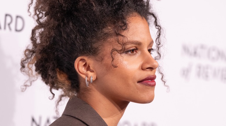 Close up of side profile of Zazie Beetz with her curly hair tied up on top of her head.