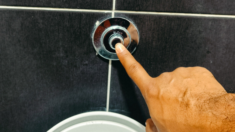 person pushing flush button for toilet