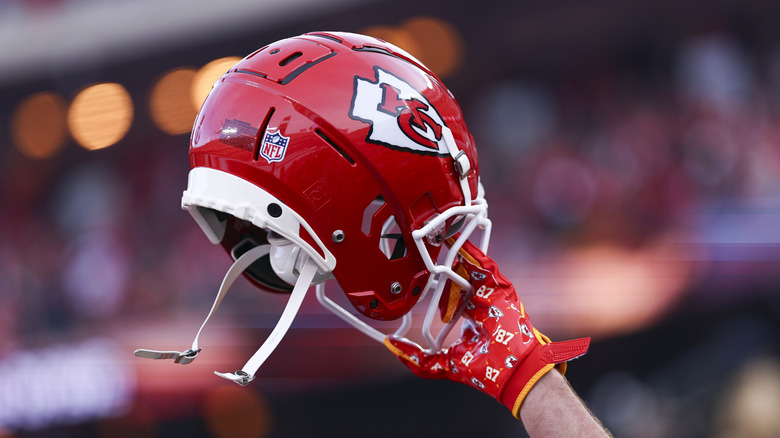Travis Kelce's hand holding up his Kansas City Chiefs helmet during a game