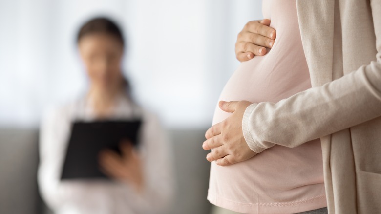 close-up of a pregnant belly with doctor in background