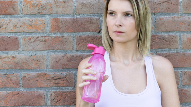 woman holding a reusable water bottle standing against a brick wall outdoors