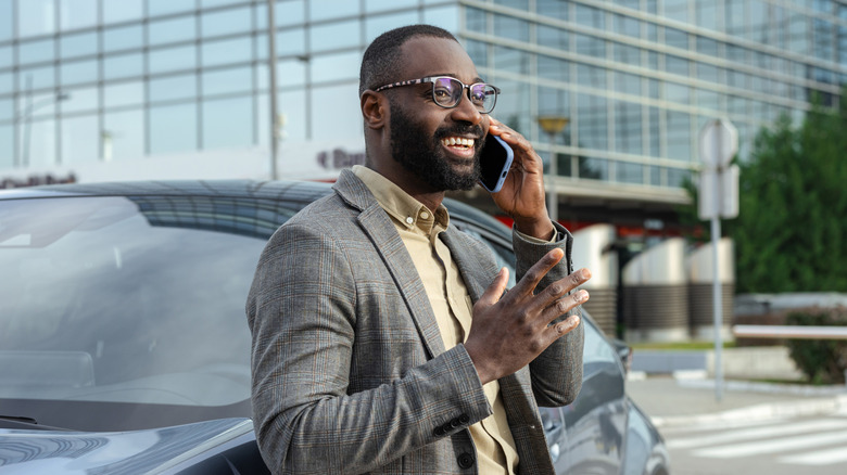 man outside leaning on car and talking on phone