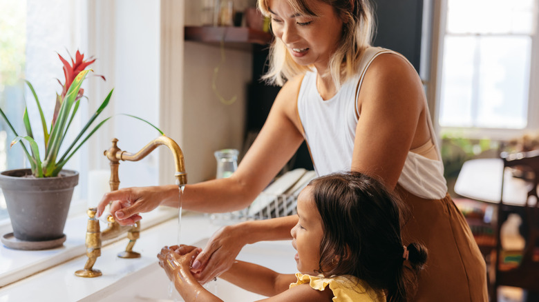 woman and child washing hands at kitchen sink
