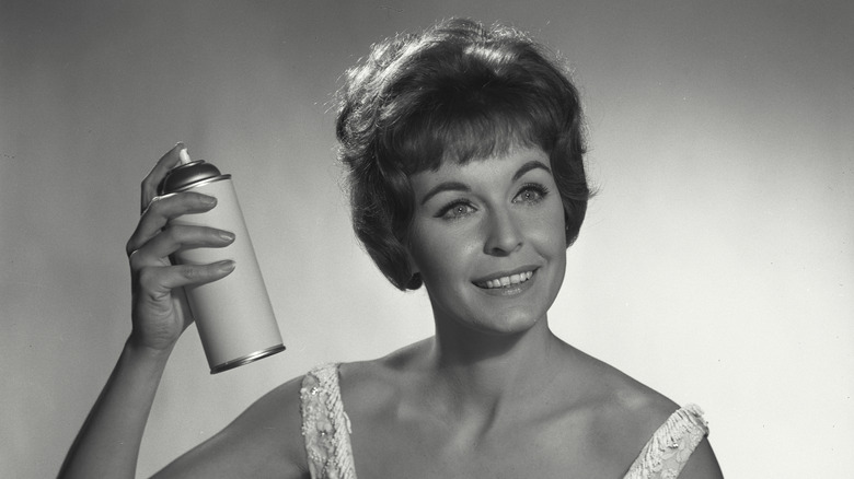 A woman spraying hairspray in her hair.