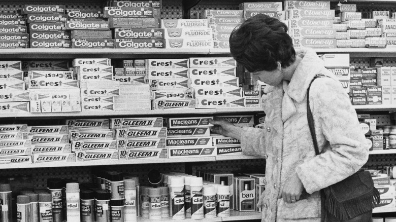 A woman inspecting the range of toothpaste on the shelves of the toiletries aisle in a supermarket