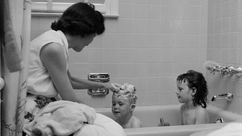 A mother shampooing her children's hair in the bath.