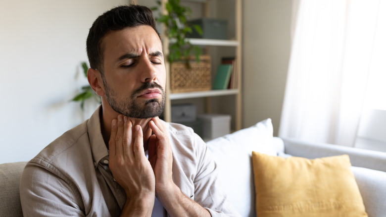 Man in pain with sore throat touching his neck