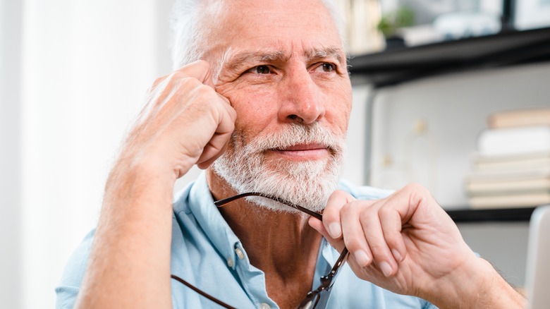 A older man sitting at a desk holding a pair of glasses