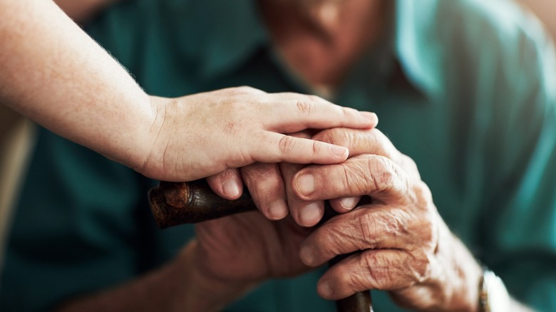 An older person with aged hands holding hands with a younger person