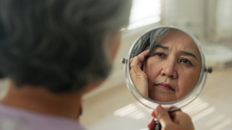 A woman looking in the mirror at her face, concerned about aging