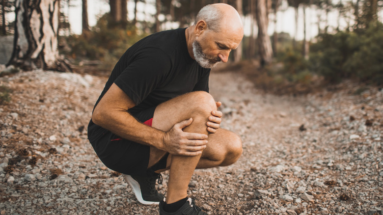 A man outdoors reaching down and grabbing his knee in discomfort