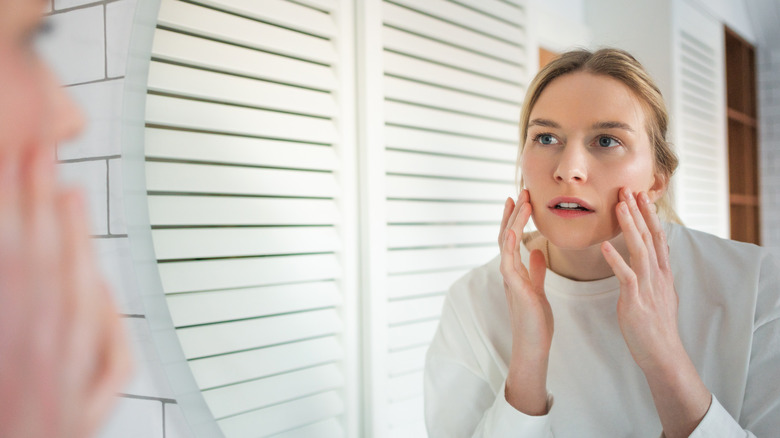 A woman looking in the mirror at her face and checking her skin