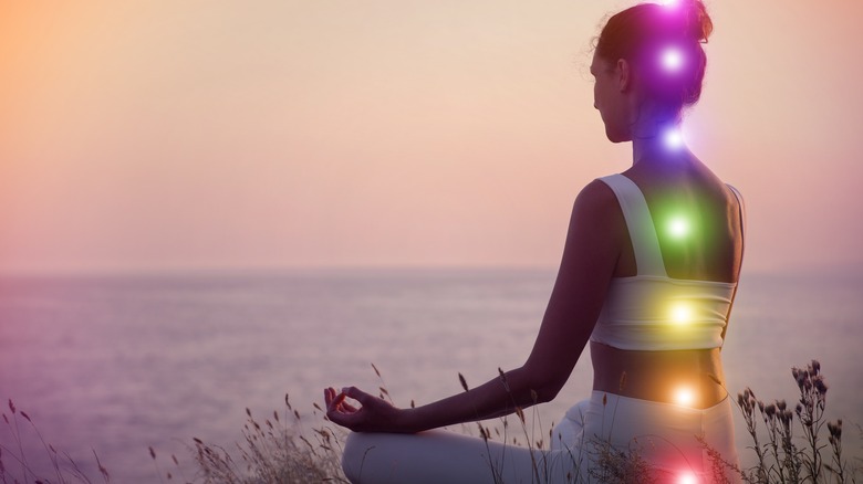 a woman sits on beach with chakra illuminated