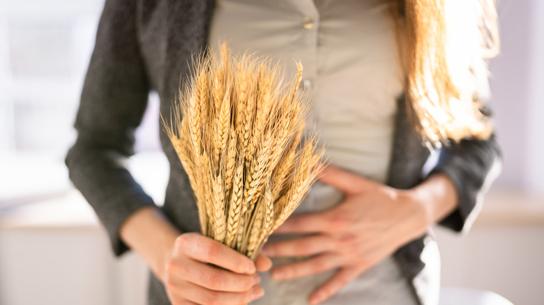 woman holding spikelet of wheat and putting hand on gut, gluten intolerance
