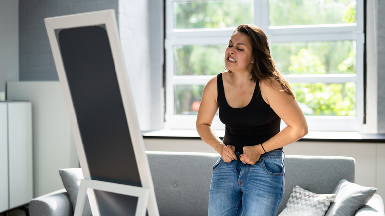 woman struggling to button her jeans