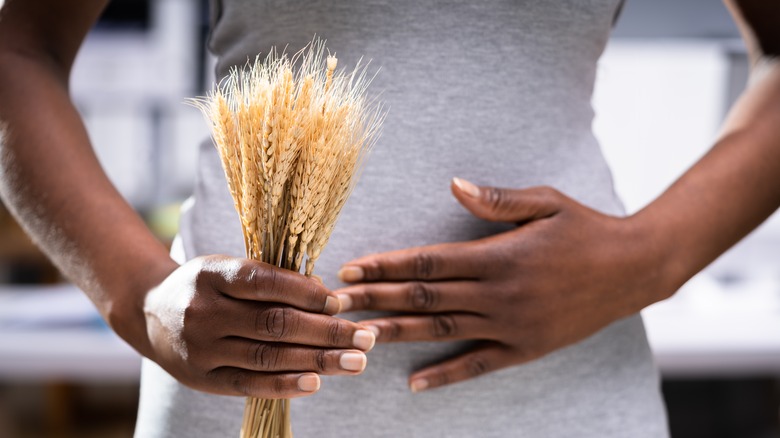 Woman with stomach upset holding stalk of wheat