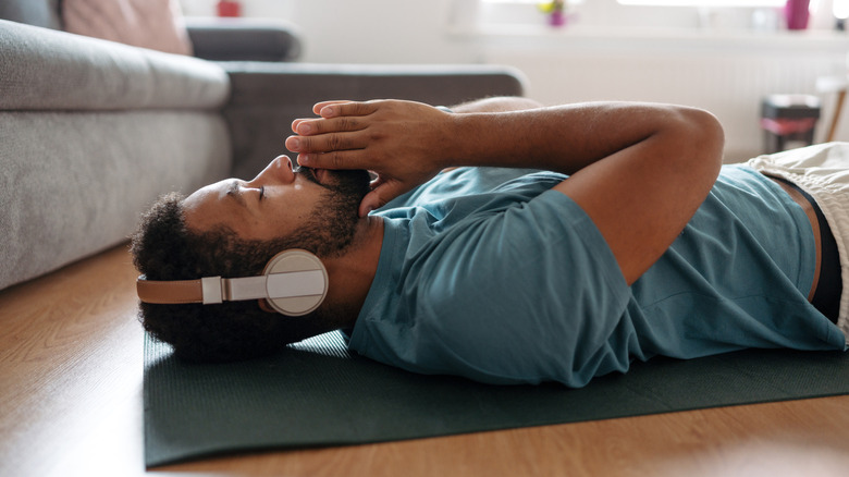 man with headphones meditating on mat at home