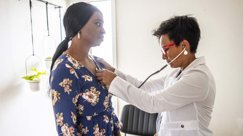 female doctor listening to heart of female patient