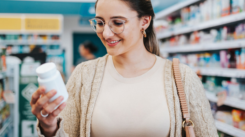 young woman looking at supplement bottle in store