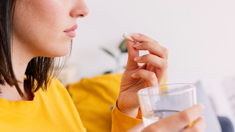 young adult woman taking a pill with water glass