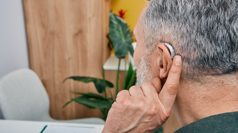 Man presses his finger to hearing aid