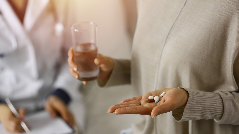 Woman holding glass of water and pills