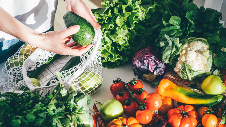 A woman unpacking an avocado from her grocery bag with an array of vegetables