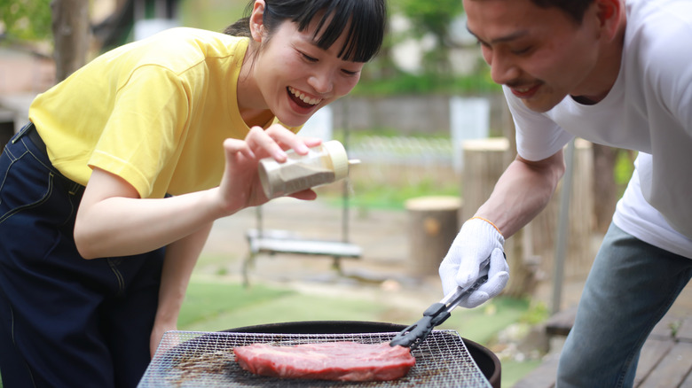 young couple cooking steak on outside grill