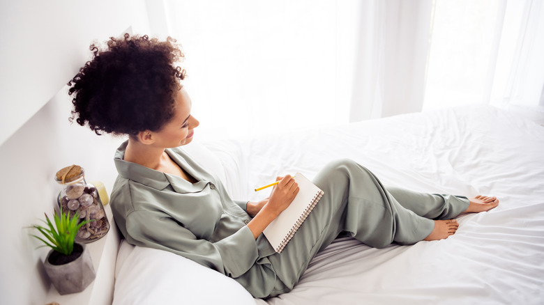 A woman in her pajamas sitting in bed and writing in a journal