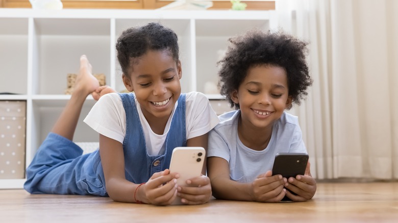 two young kids smiling while using their phones