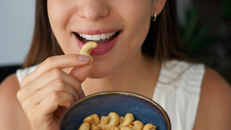 woman putting cashew into her mouth from bowl