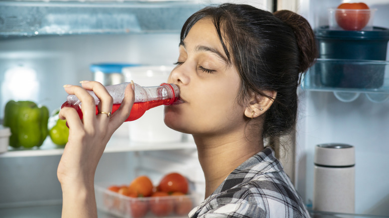 young woman drinking red juice from refrigerator