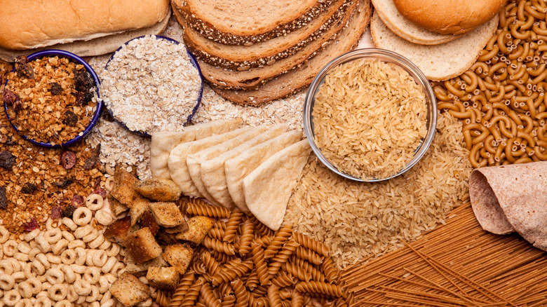 Whole grain bread, cereal, oats, rice, and pasta in bowls and spread out on a surface