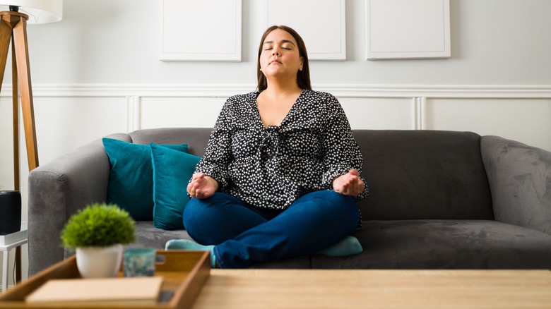 Woman sits on couch meditating