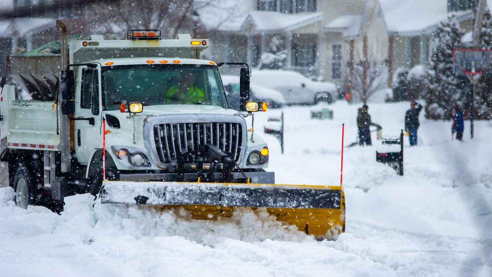 Snow plow going down snow-covered road with people in background