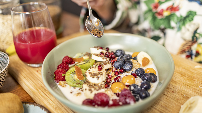 A spoonful of flaxseeds sprinkling over a bowlful of yogurt and fruit