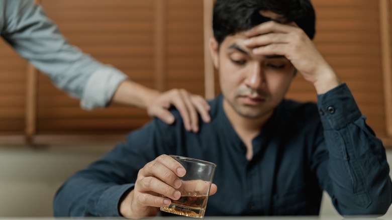 man drinking alcohol with someone's hand on his shoulder