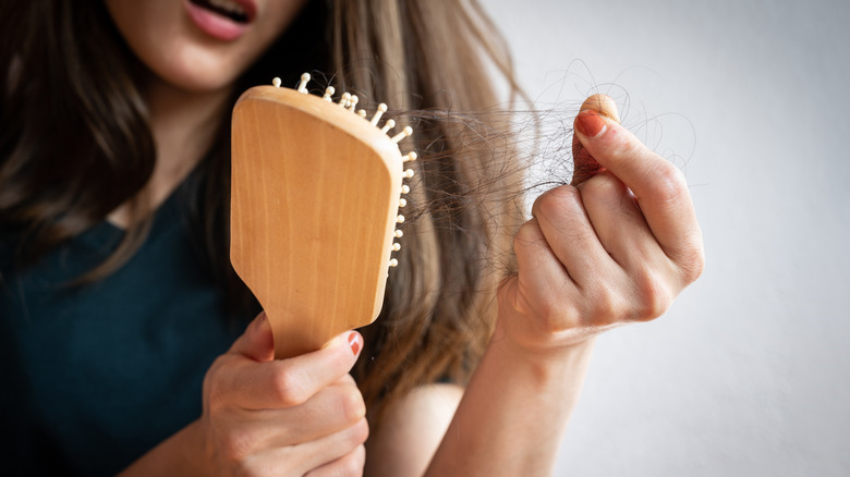 woman looks appaled as she pulls hair from her hairbrush 