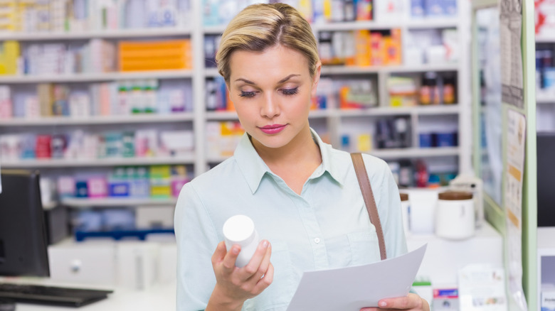 A woman looking at her prescription bottle and information insert while at the pharmacy